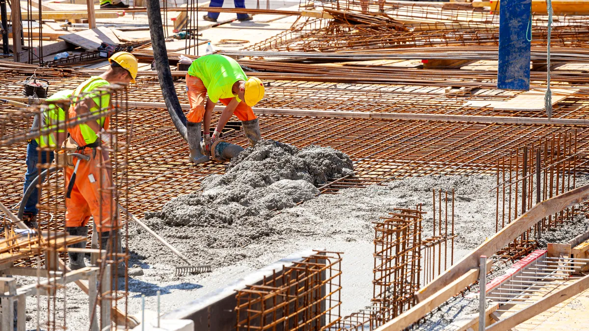 Workers in yellow vests and hard hats pouring concrete on a construction site.