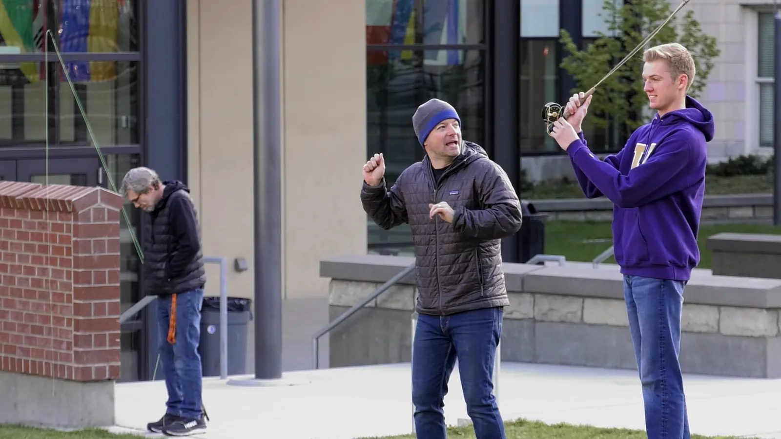 Three people are standing outside with one person casting a fishing line.