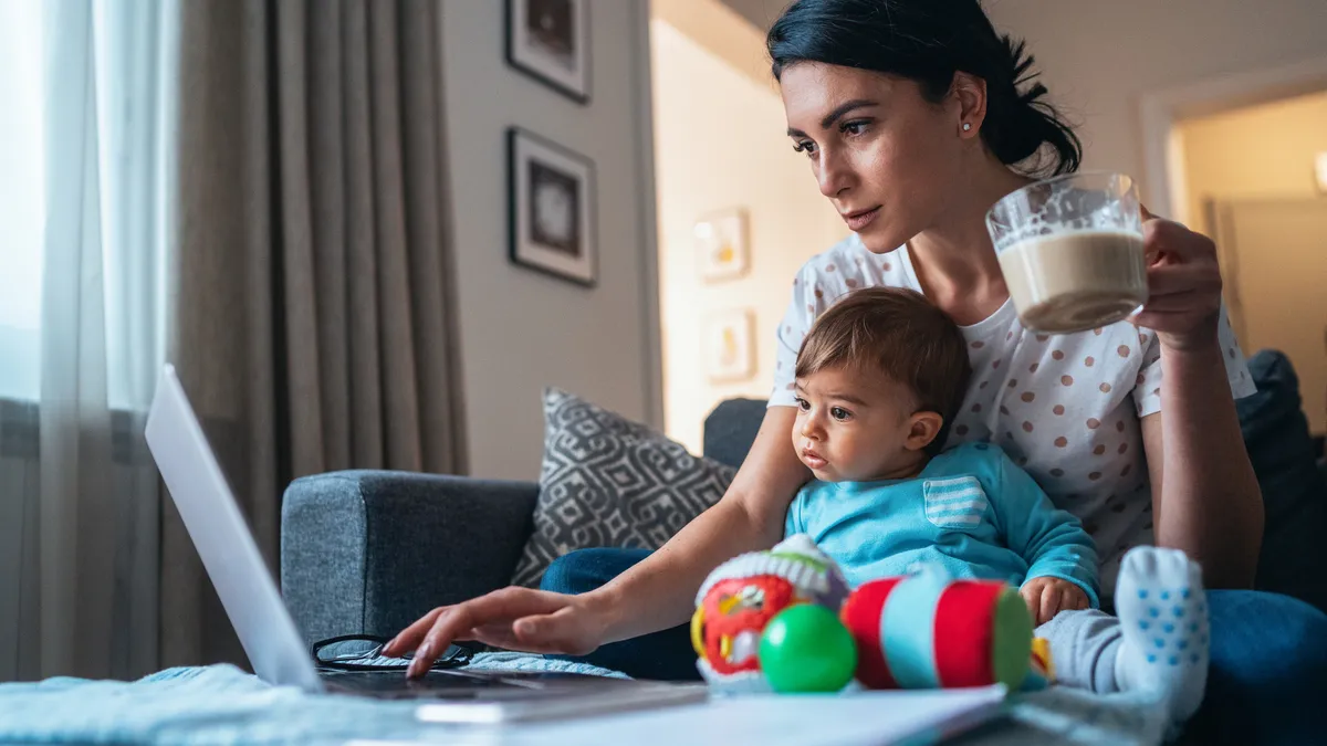 Young modern mother with a baby using laptop at home