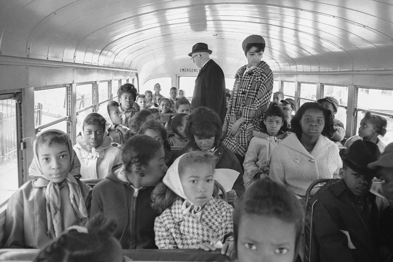 Two adults overlook rows of Black children sitting on a school bus