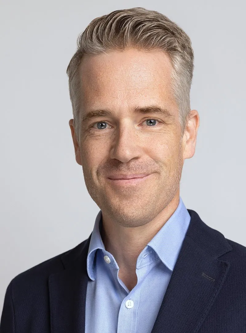 A close-up of a person in business attire looking straight ahead.