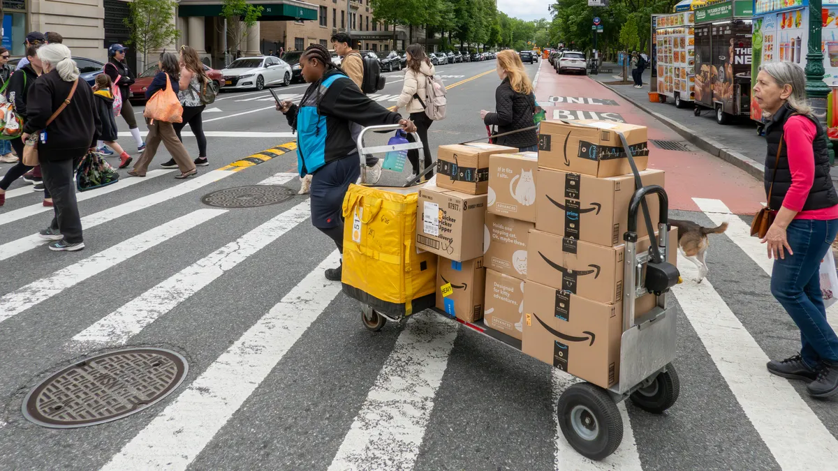 A person pulls a trolley with Amazon packages across the street at a crossing.