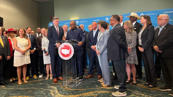 A large group of people stand around one person at a podium.