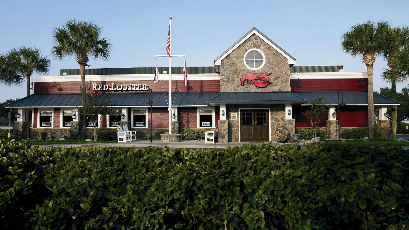 An exterior shot of a Red Lobster restaurant from downhill, in the foreground, lush shrubbery separates the restaurant from the camera.