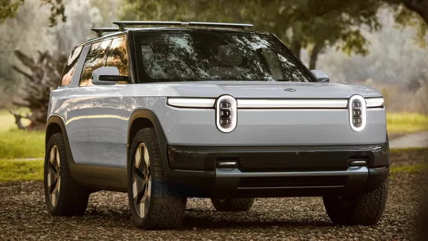 A white Rivian R2 electric SUV parked outdoors with fallen leaves on the ground.