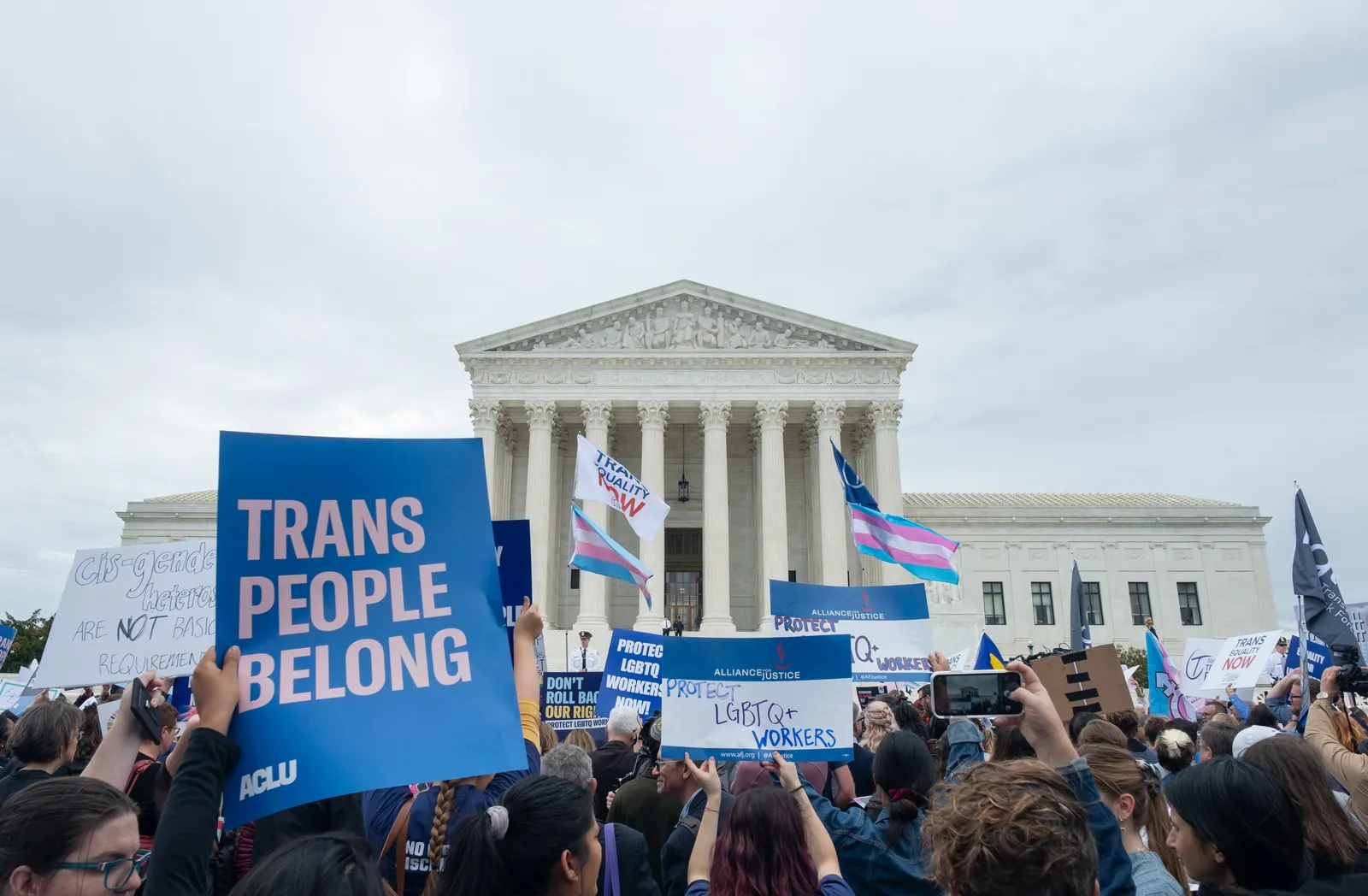 Individuals stand outside the U.S. Supreme Court. A sign reads &quot;Trans People Belong.&quot;