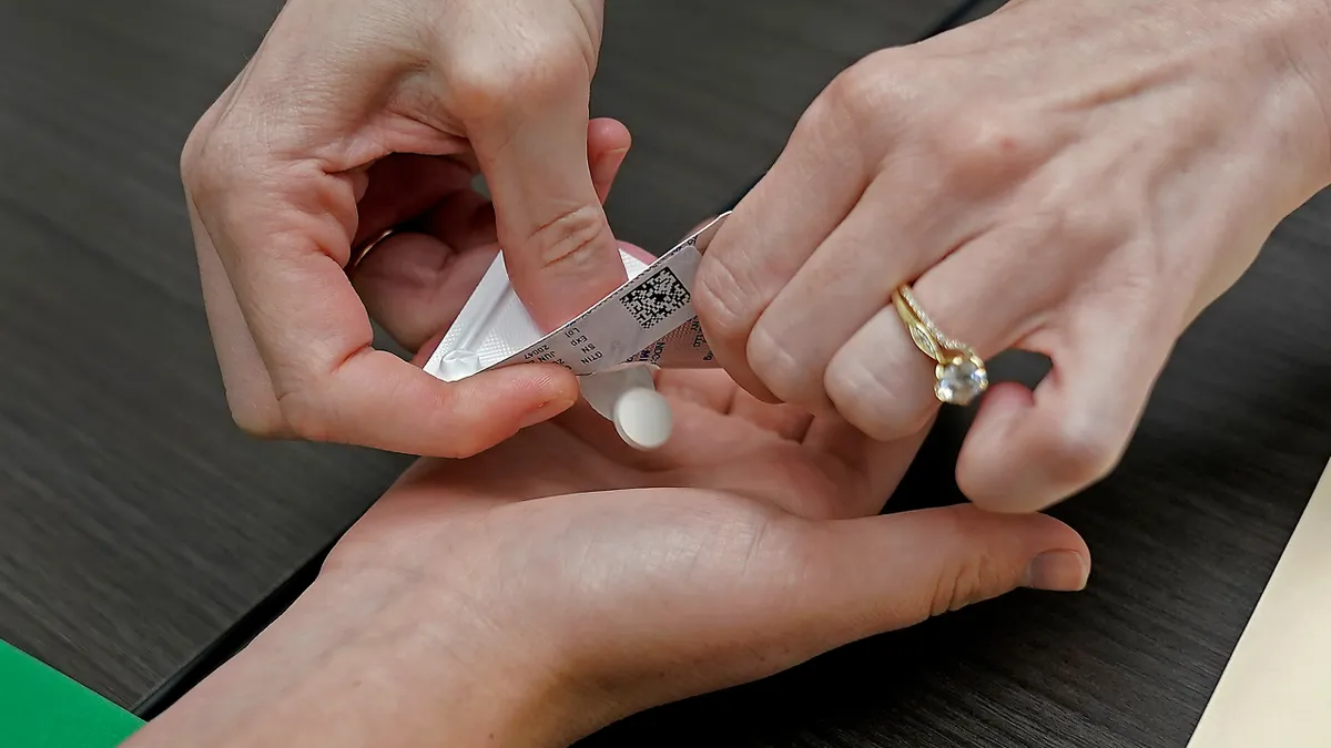 A picture of someone dispensing the abortion pill, mifepristone, into a person's outstretched hand.