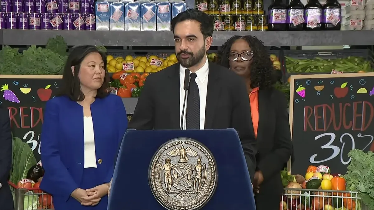New York City Mayor Zohran Mamdani speaks in front of a sign that says "Reduced 30%."