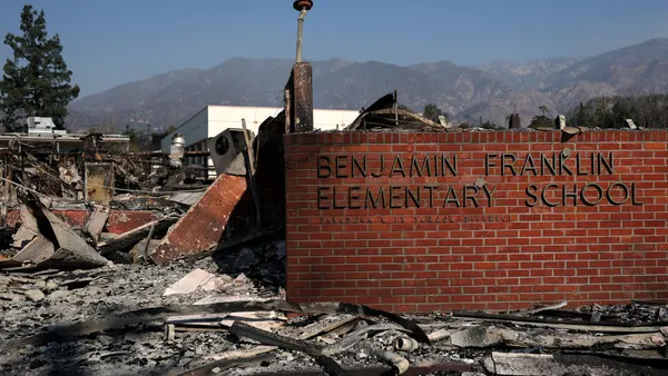 A brick wall with the name of an elementary stands among fire scorched landscape