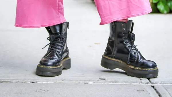 A closeup of a person's outfit holding a black Gucci bag and wearing Dr. Martens boots.