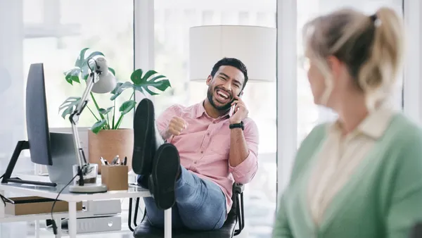 A person in the foreground looks back at another talking on a phone call with feet up.