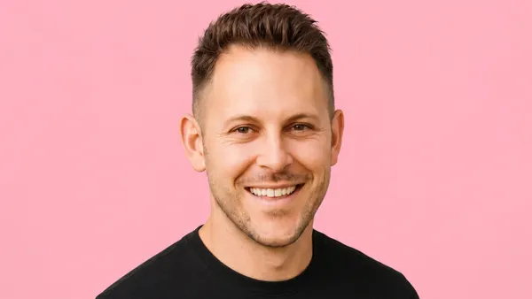 A smiling white man in a black t-shirt in front of a pink background