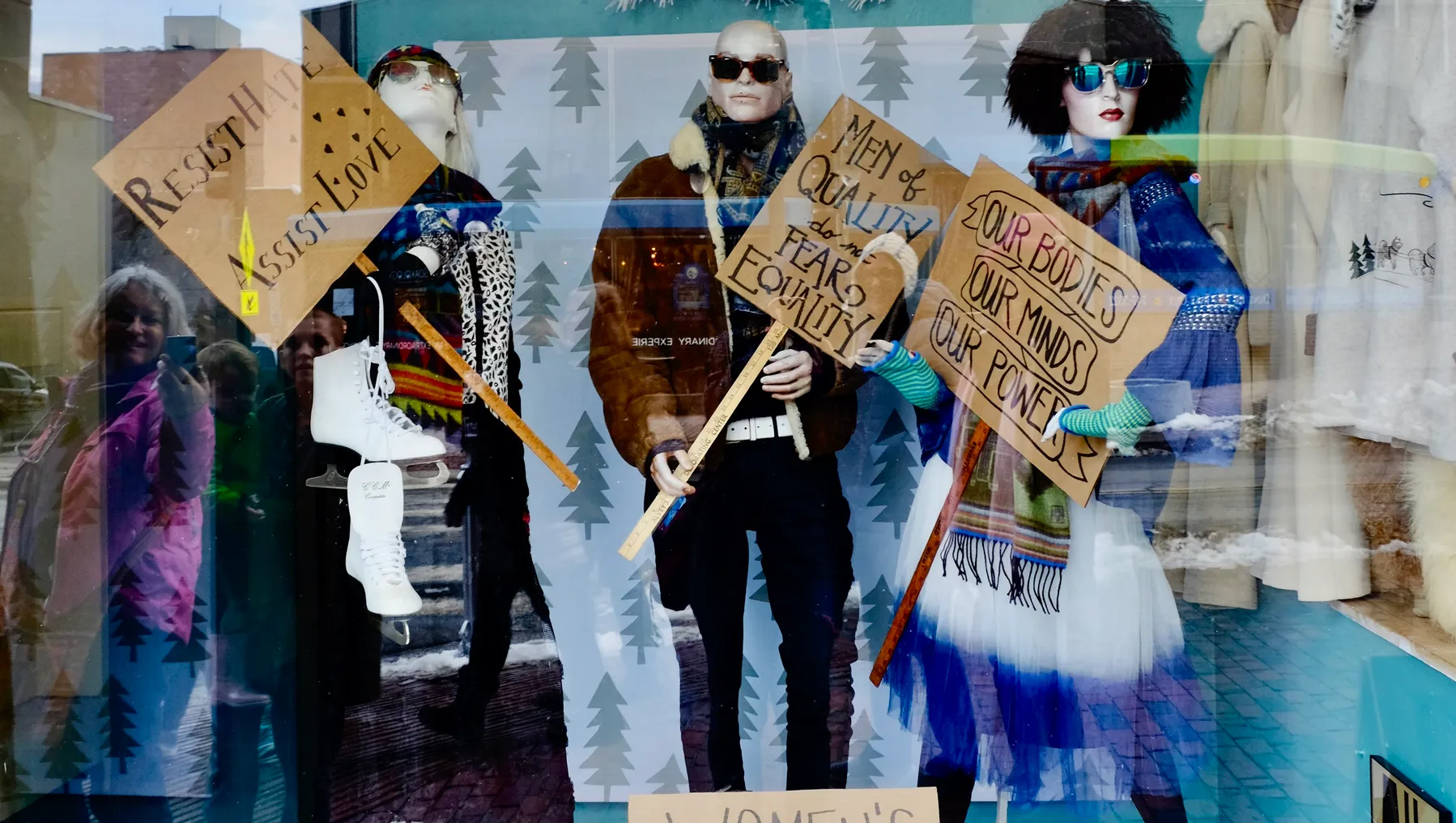 A resale boutique window features mannequins wearing secondhand clothing and holding handwritten signs touting civil rights.