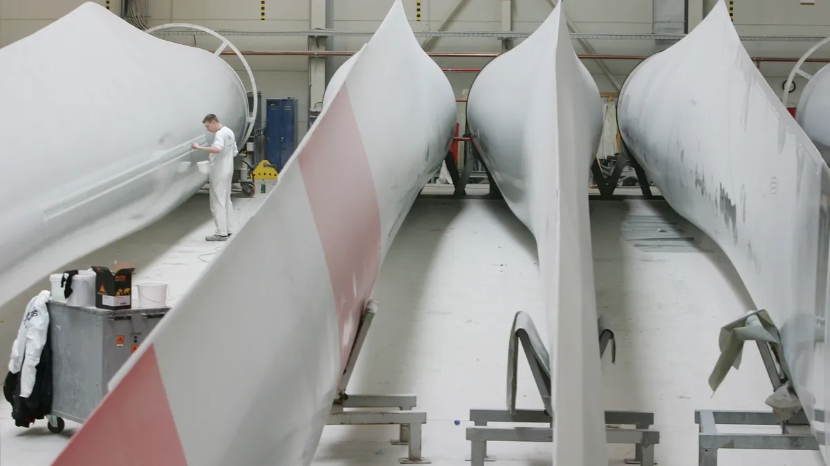 A factory worker examines a wind turbine blade.