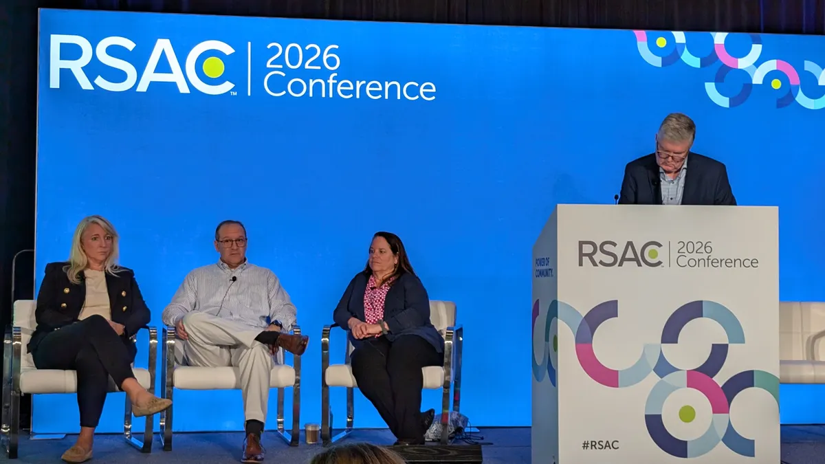 Three people sit and one person stands on a stage with a backdrop reading "RSAC 2026 Conference"