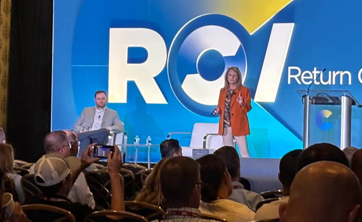 A photo of two people speaking top a crowd from a stage.