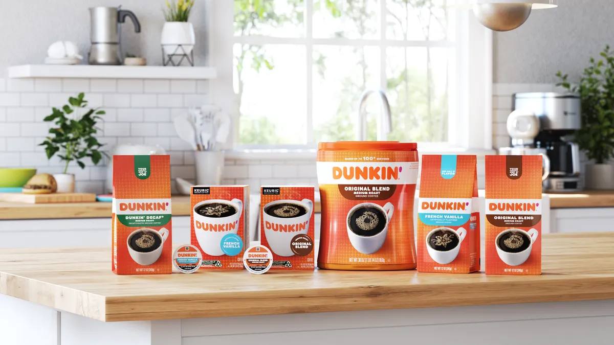 A lineup of Dunkin' coffee CPG products, including beans, grounds and K-Cup products, on a wooden countertop in a fairly white kitchen.