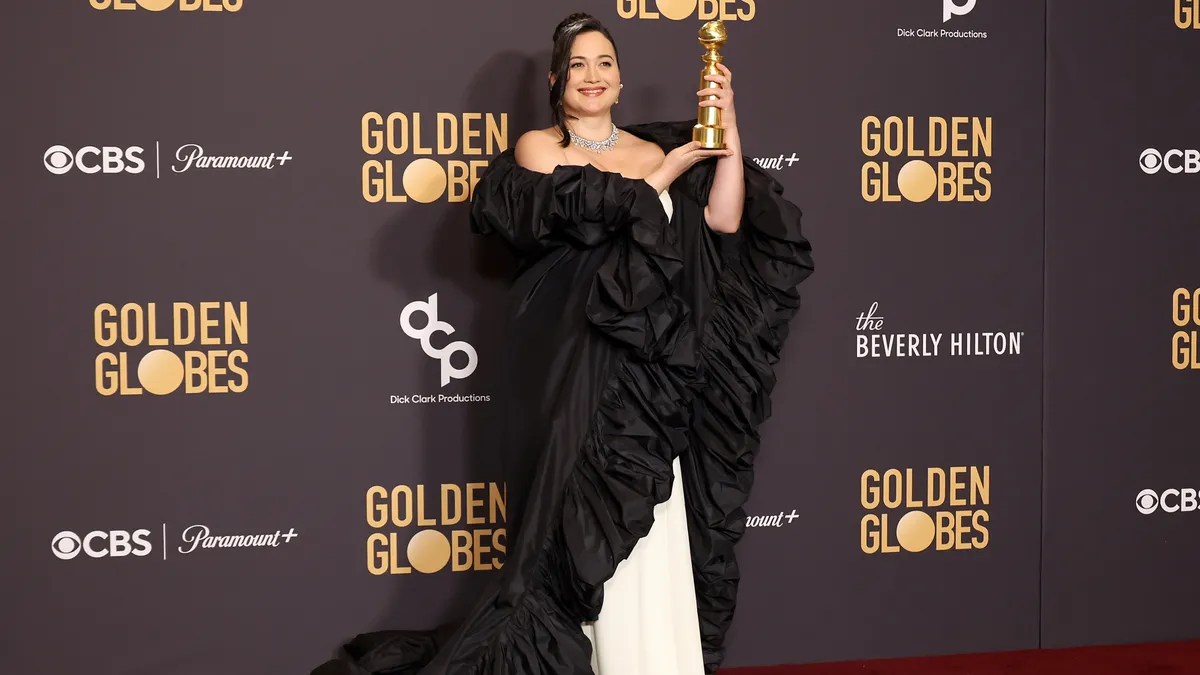 Actor Lily Gladstone wears a long black satin ruffled shawl and holds up her Golden Globe award.