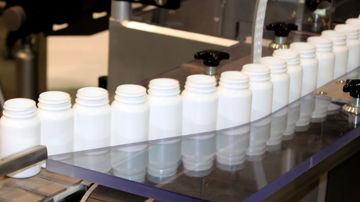 Dozens of unfilled plastic bottles, such as those for holding over-the-counter medication, on an industrial conveyor.