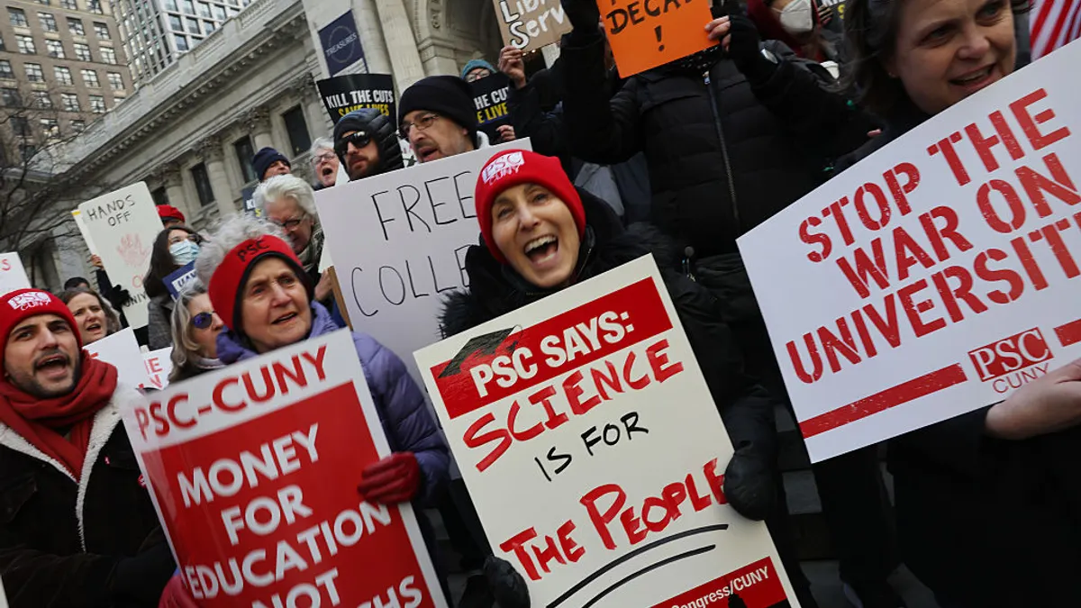 A group of people are outside holding signs opposing cuts to education research