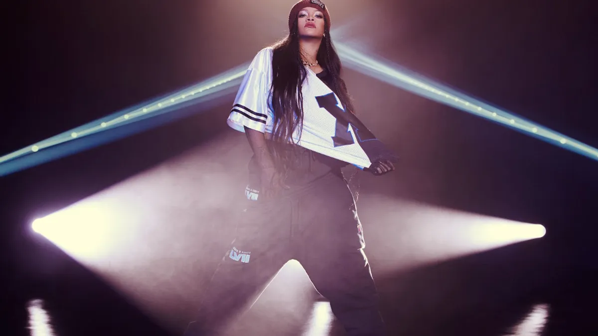 Rihanna stands in the middle of a stage with lights on her.