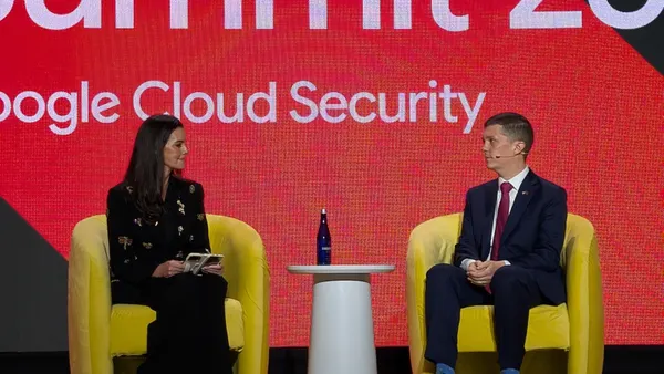 A woman and a man sit in yellow chairs on a conference stage