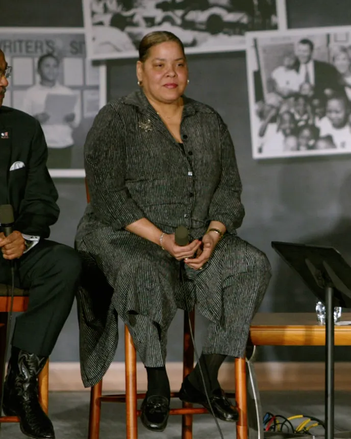 A woman in a dress sits on a brown stool with images posted behind her.