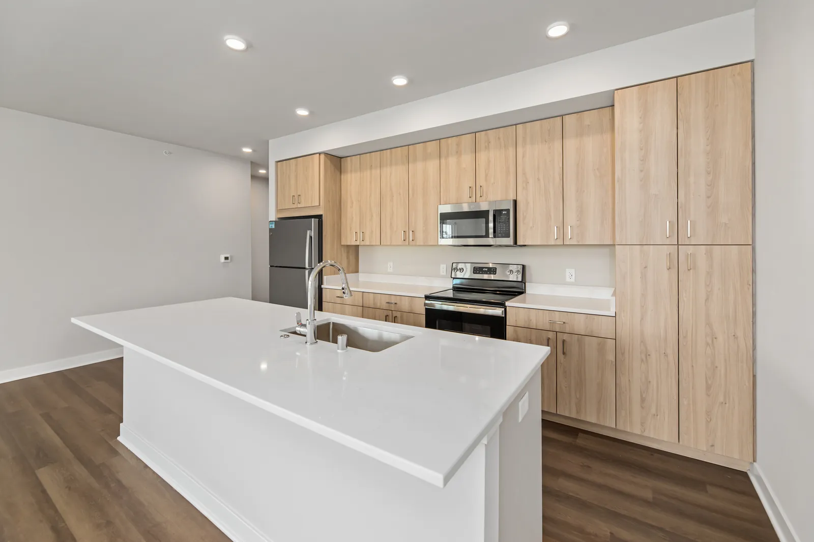 A kitchen with wood-look flooring, a white kitchen island and stainless steel appliances.