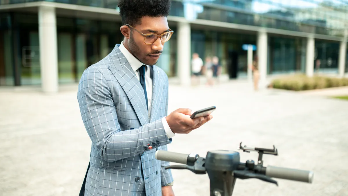 A person in a suit using a smartphone app to access a shared electric scooter.