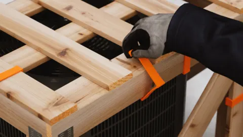 A person&#x27;s hand touches an orange plastic fastener on a wooden crate.