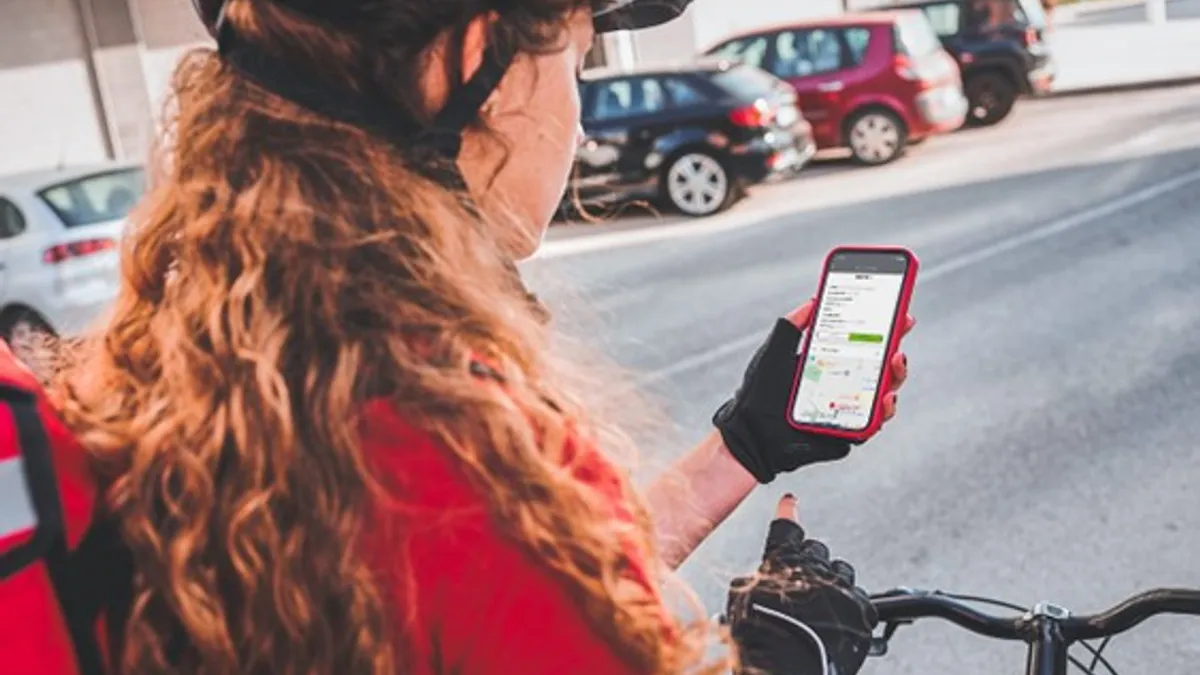 A delivery person on a bicycle checks the address of their next shipment with their mobile phone.