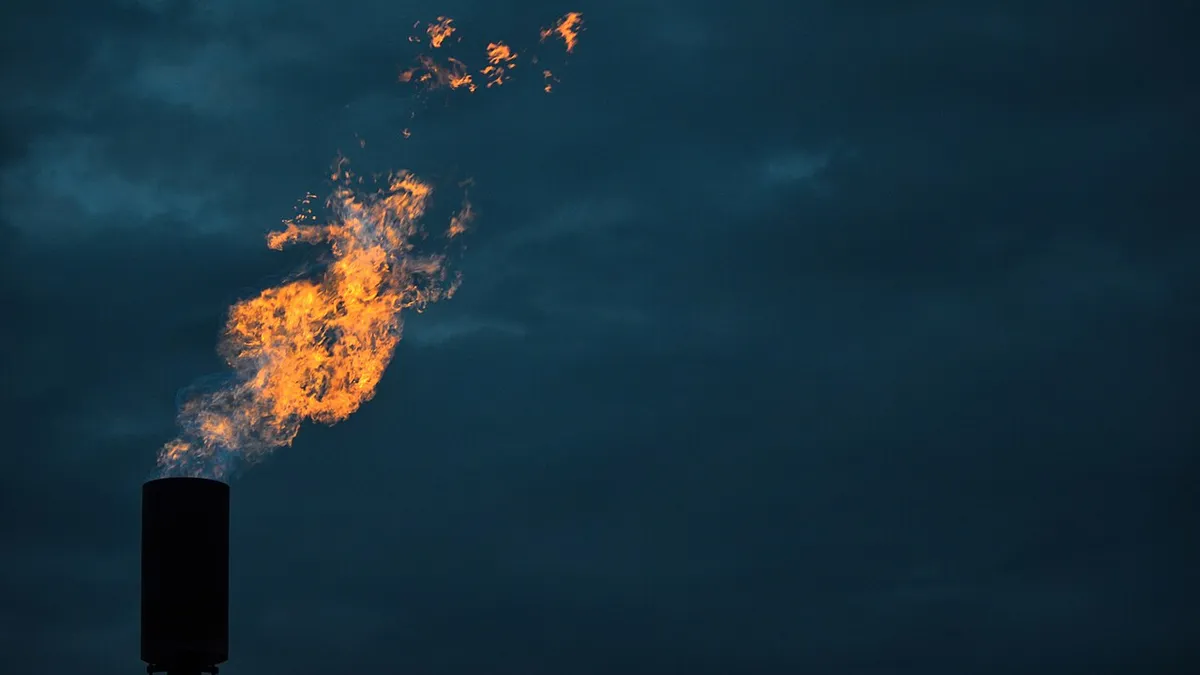 A flame burns out of a metal stack against a dark sky