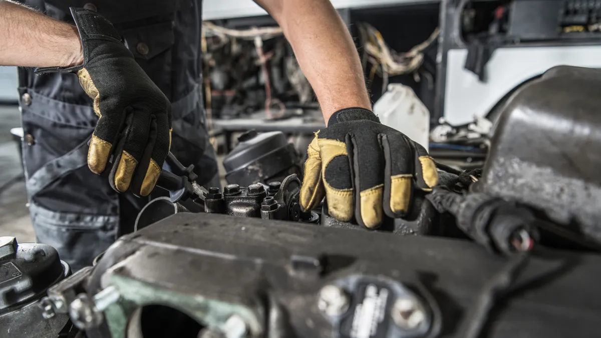 A mechanic wearing black and yellow gloves works on a truck.