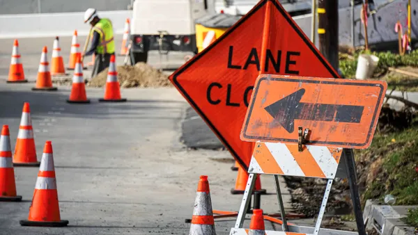 Several bright signs and cones indicate a lane is closed for construction work.