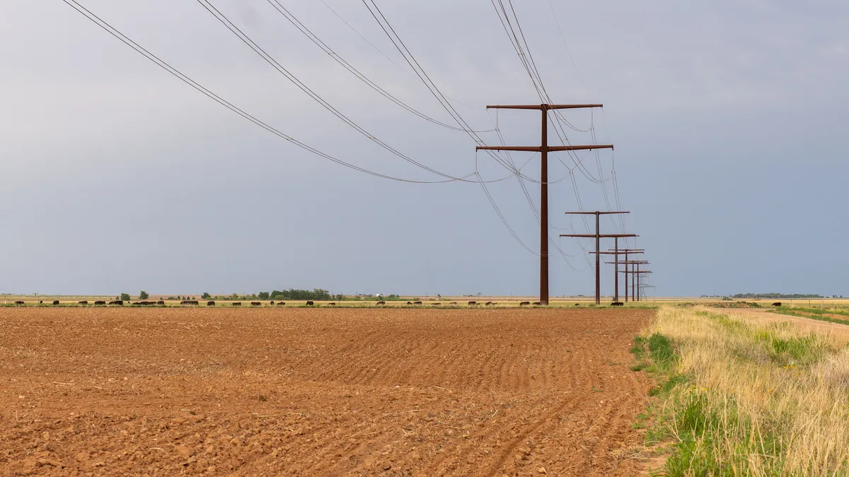 High-voltage power lines crossing a plowed field.