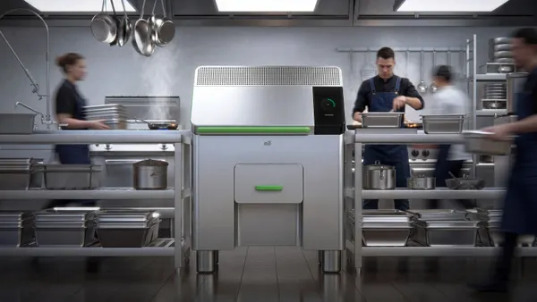 A stainless steel machine with a handle and the Mill logo sits in the middle of a busy kitchen.