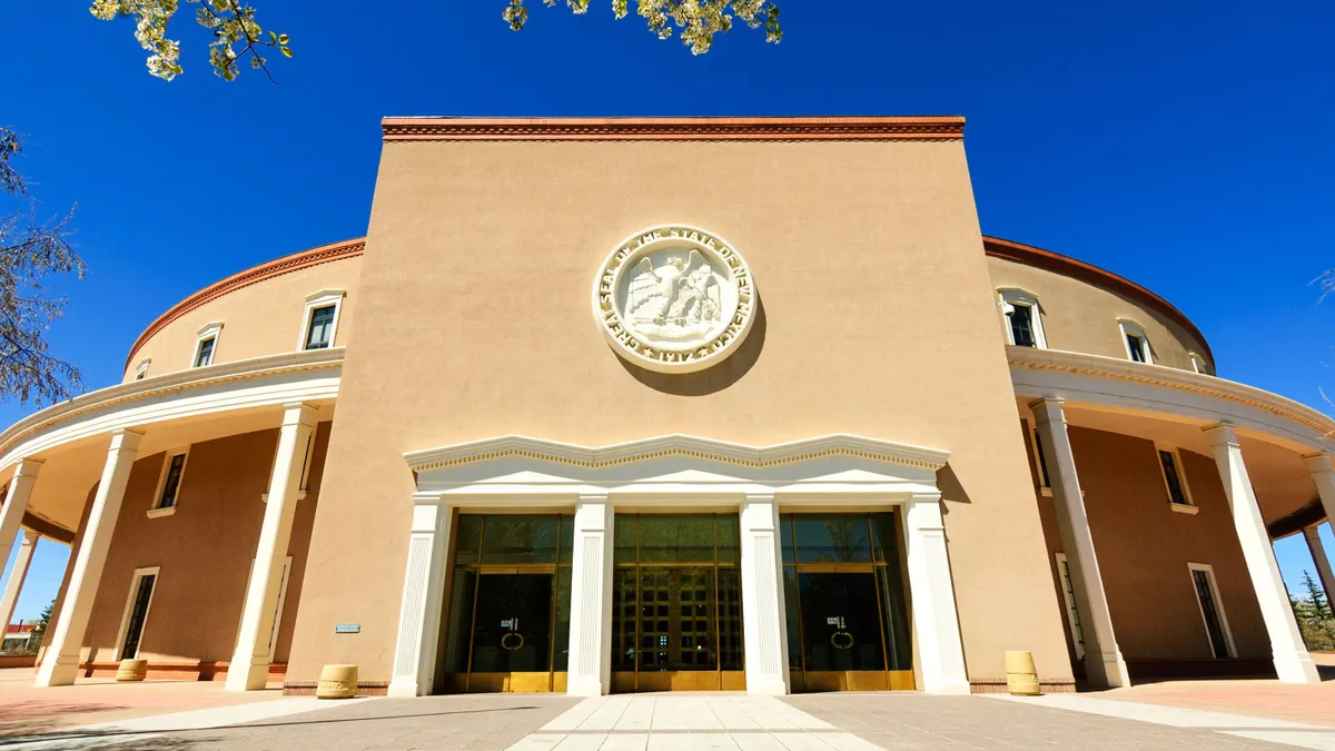 Exterior of the New Mexico state capitol building, which is stucco and prominently features the state seal.