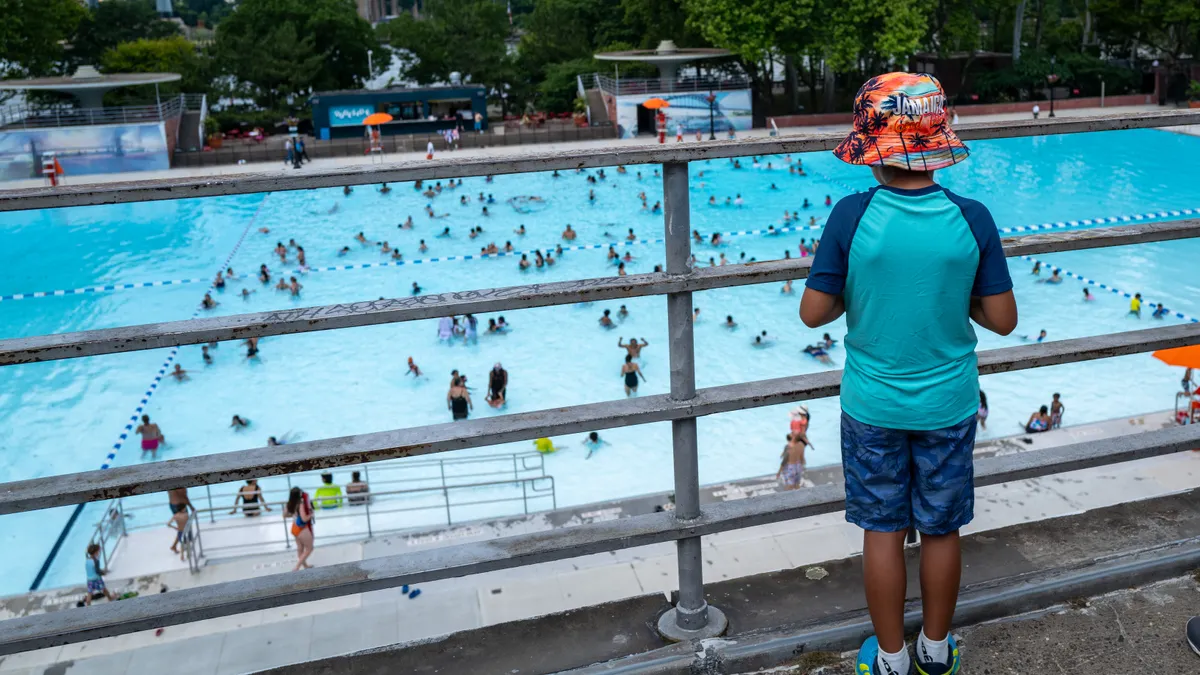 A child watches as people enjoy a municipal swimming pool.