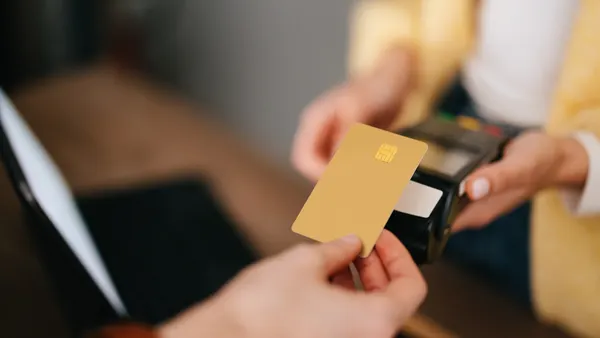 From above photo of an anonymous woman holding credit card reader while African-American customer paying bill using contactless payment.