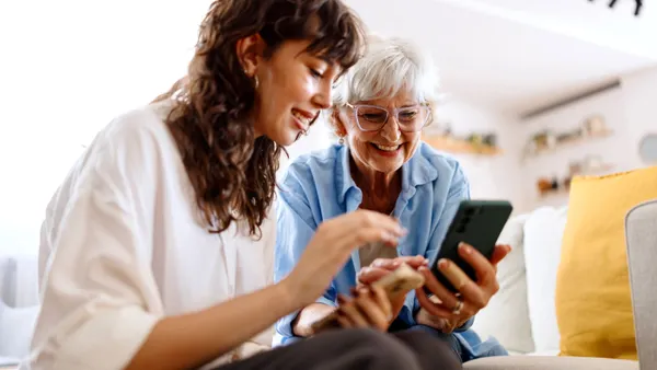 A woman shows an older woman something on a smartphone.