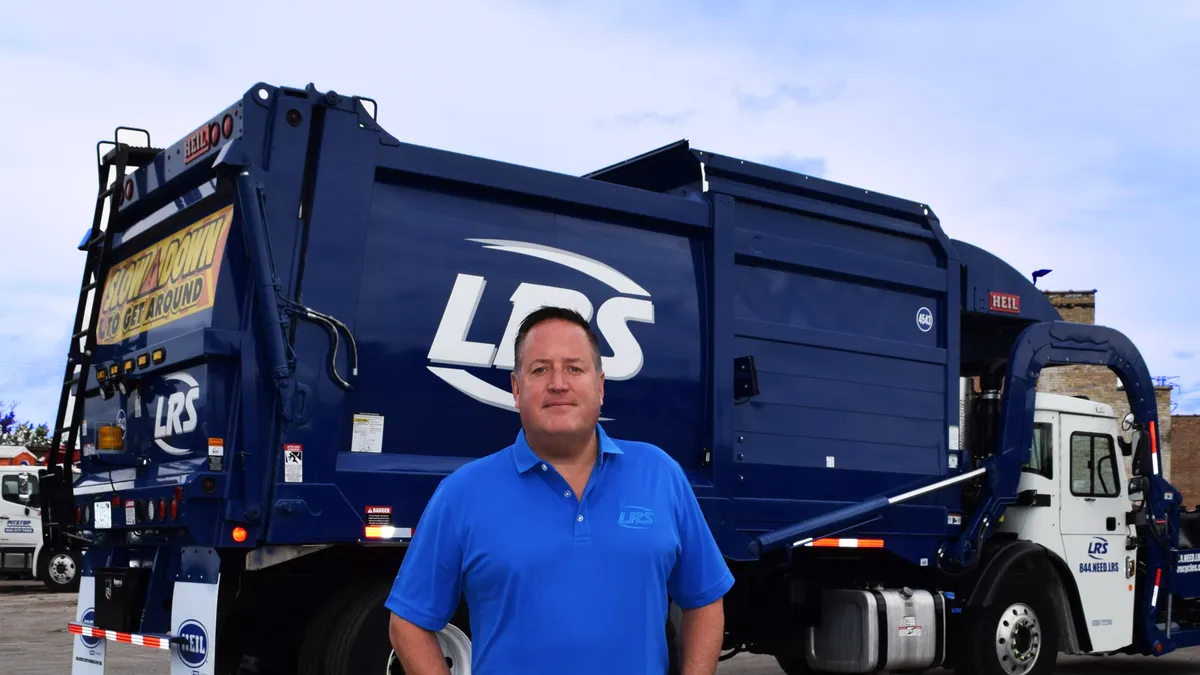 Man in blue polo standing in front of blue garbage truck