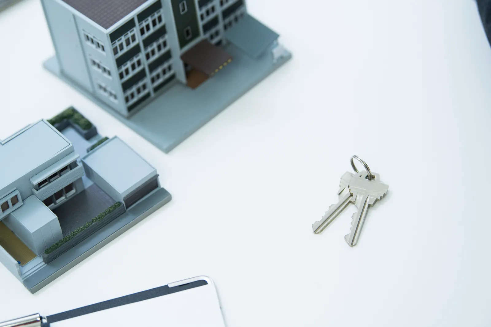 Two models of the building, two keys of the house and a binder on the white table.