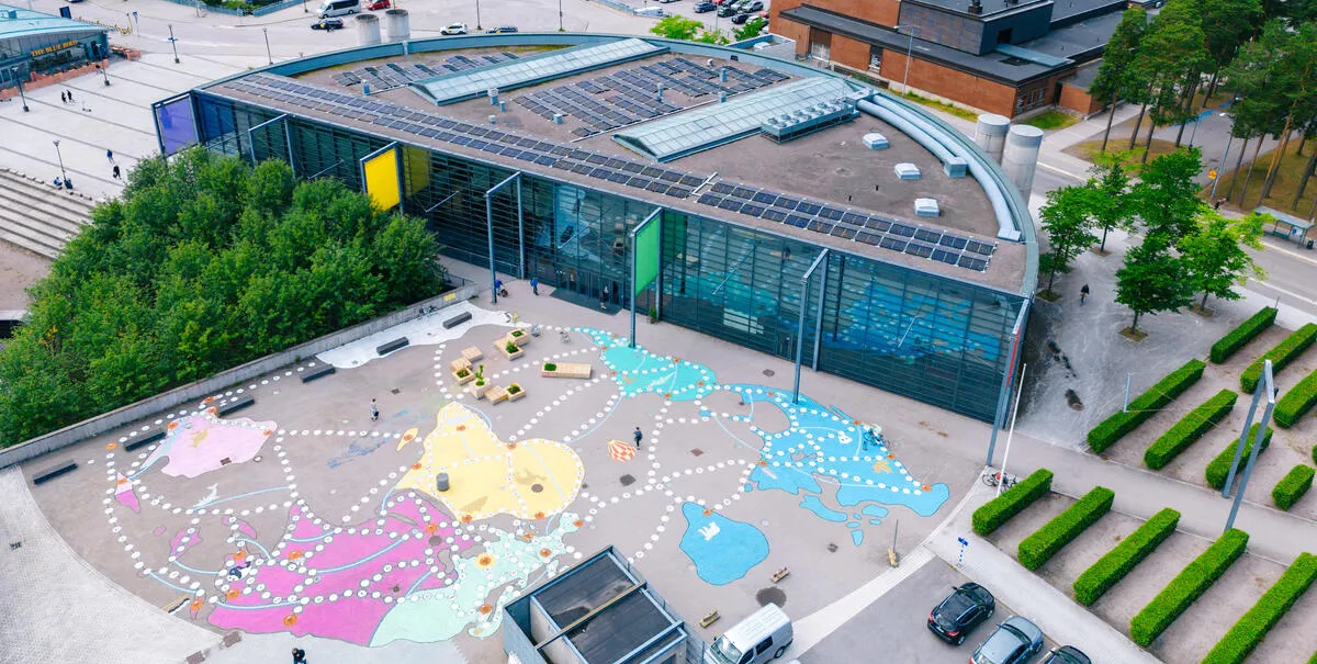 Aerial shot of painted asphalt map in front of a building shaped like half a circle