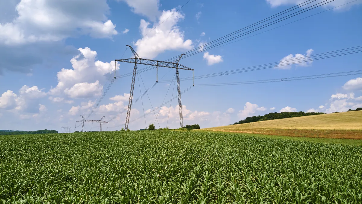 High-voltage tower with electric power lines between green agricultural fields.