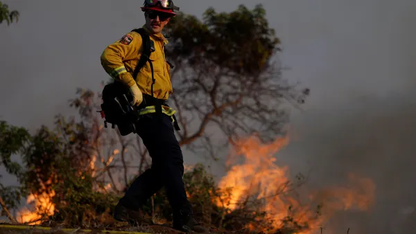 A man in wildfire gear stands near a fire.