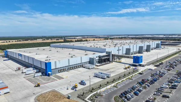 A large warehouse sits on a lot with trucks and a parking lot