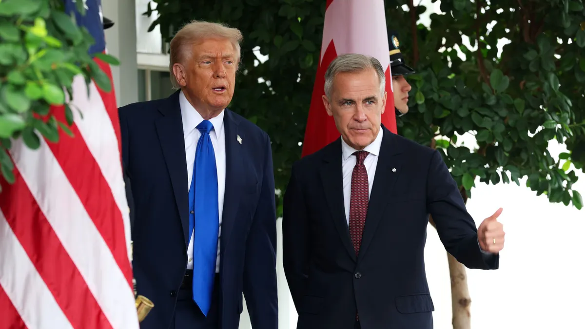 United States President Donald Trump stands next to Canada Prime Minister Mark Carney flanked by U.S. flags.