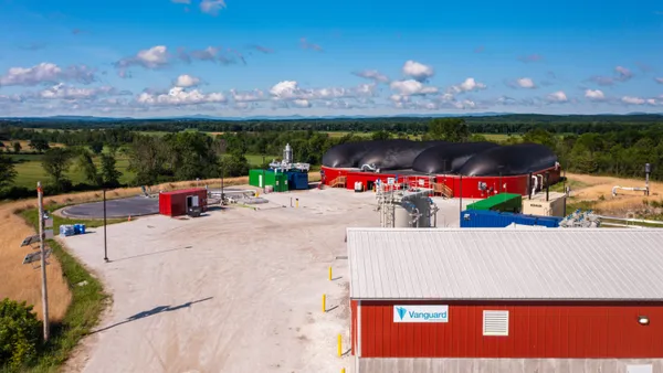 Vermont landscape, with red building in foreground, digester tanks in the middle and forest/skyline in the back.