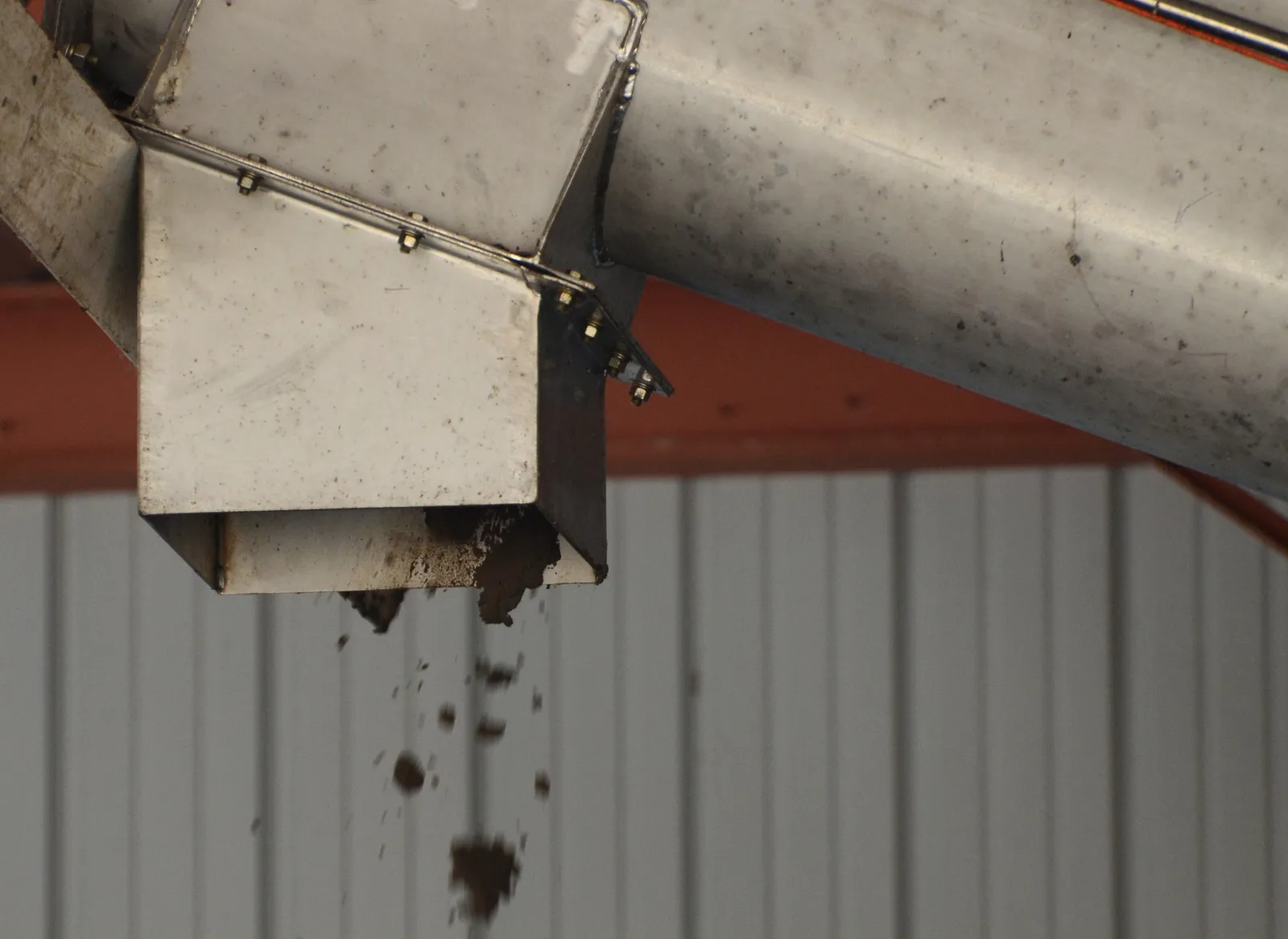 A brown earthy substance falls out of a metal pipe inside a facility.