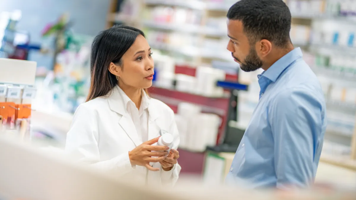 Pharmacist talking with customer about medicine bottle in drugstore.